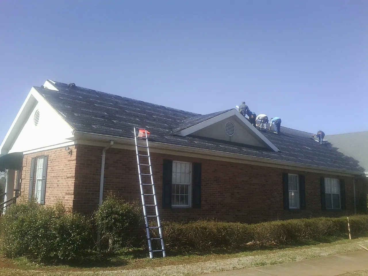 Crew tearing shingles off a brick ranch roof with a ladder set — Emergency Roof Repair work by our crew in Geigertown
