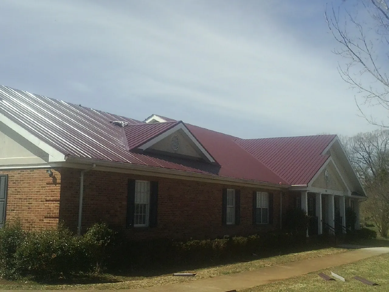 Red metal roof with gabled entries on a long brick building, from a Hail Damage Roof Repair job in Geigertown