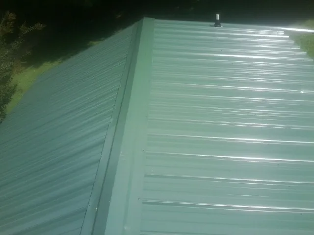 New green metal panels meeting at the ridge of a roof — Flat Roof Repair work by our crew in Geigertown
