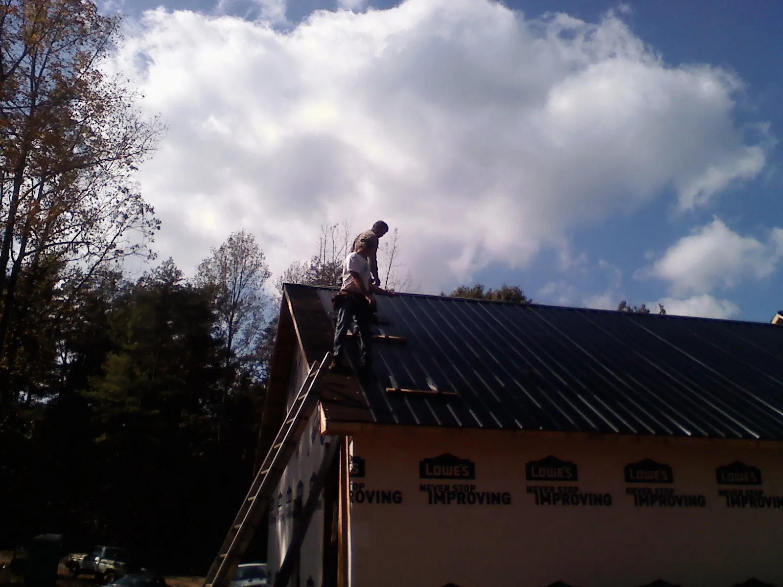 Roofer fastening dark metal panels high against a cloudy sky, from a Roof Inspection job in Geigertown