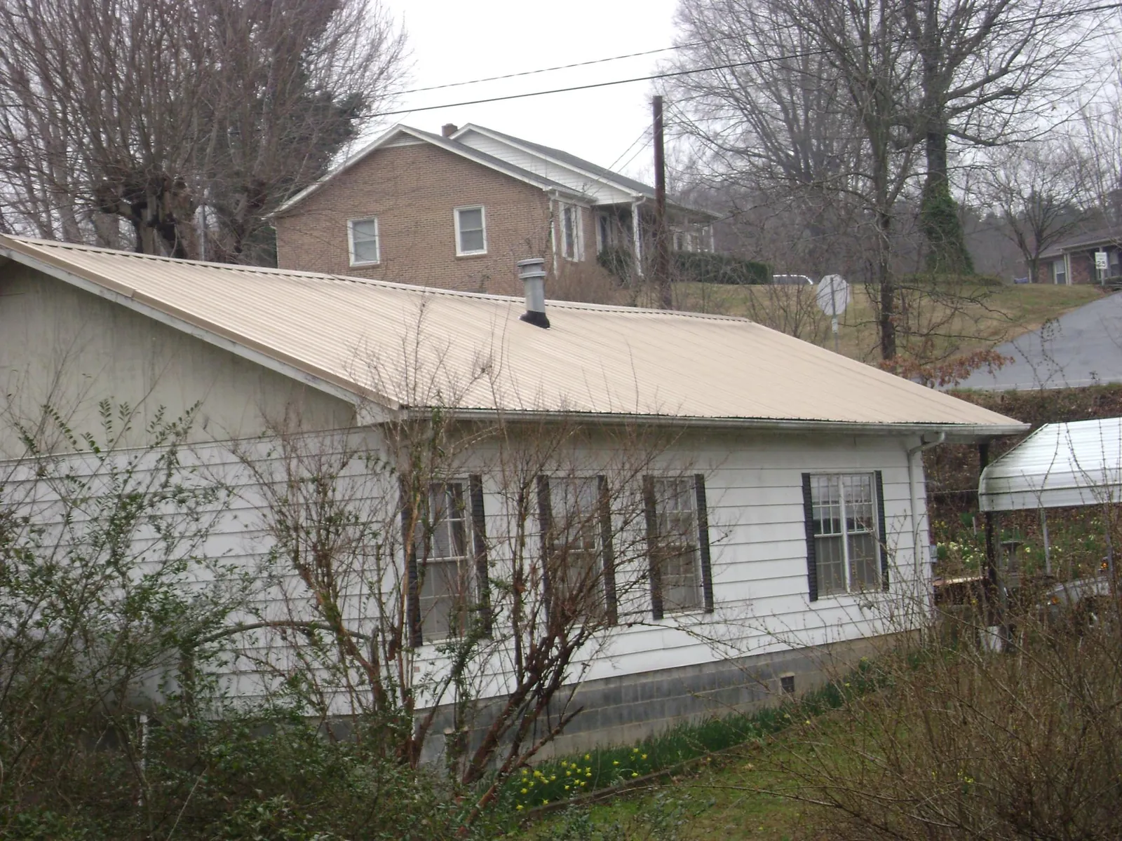 Tan metal roof on a white sided house set into a hillside — Commercial Roofing by Roofing Brothers in Geigertown